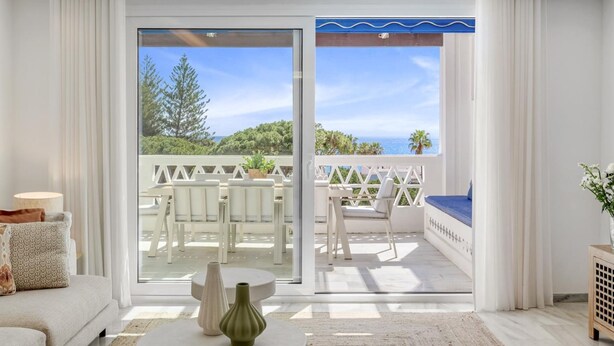 Ein modernes Wohnzimmer mit einer Couch, einem Couchtisch mit Vasen und Blick auf eine Außenpatio mit Stühlen und einem Tisch.