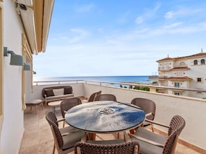 Ein Balkon mit rundem Tisch und Korbstühlen, der Blick auf die Küste freigibt.