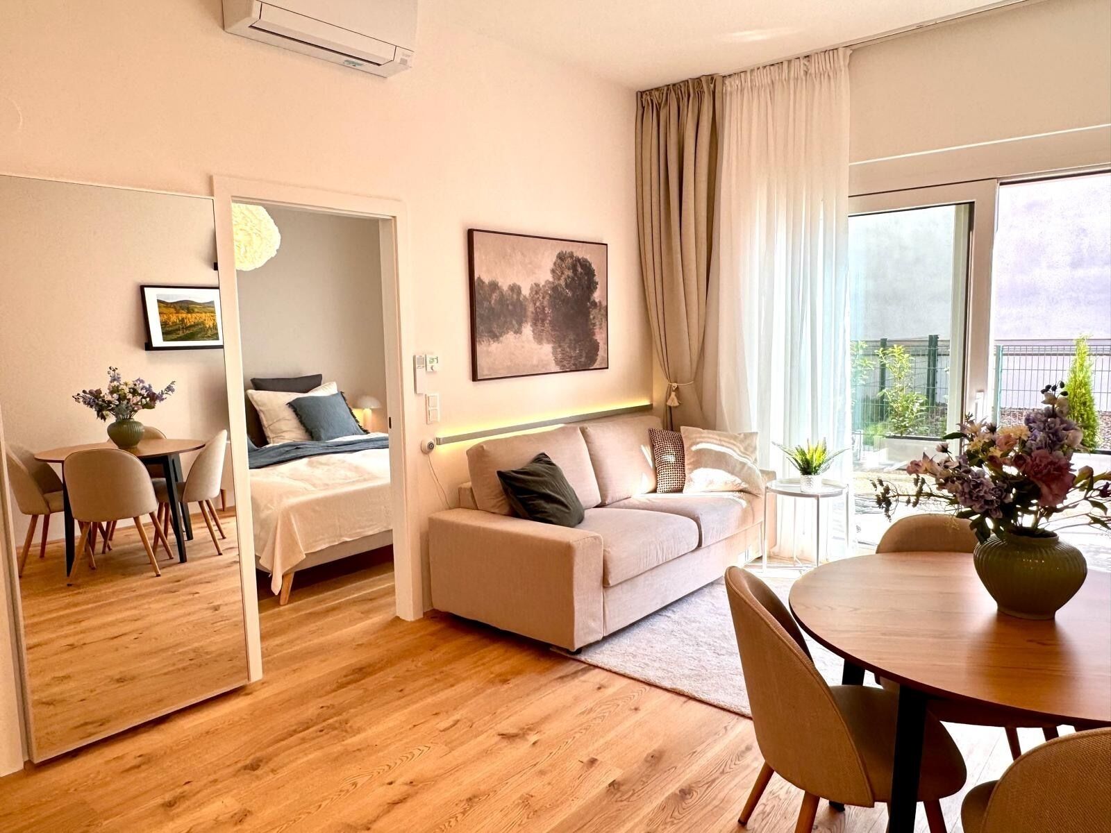 A modern living room with a sofa, a dining table, and a bed in the adjacent room.