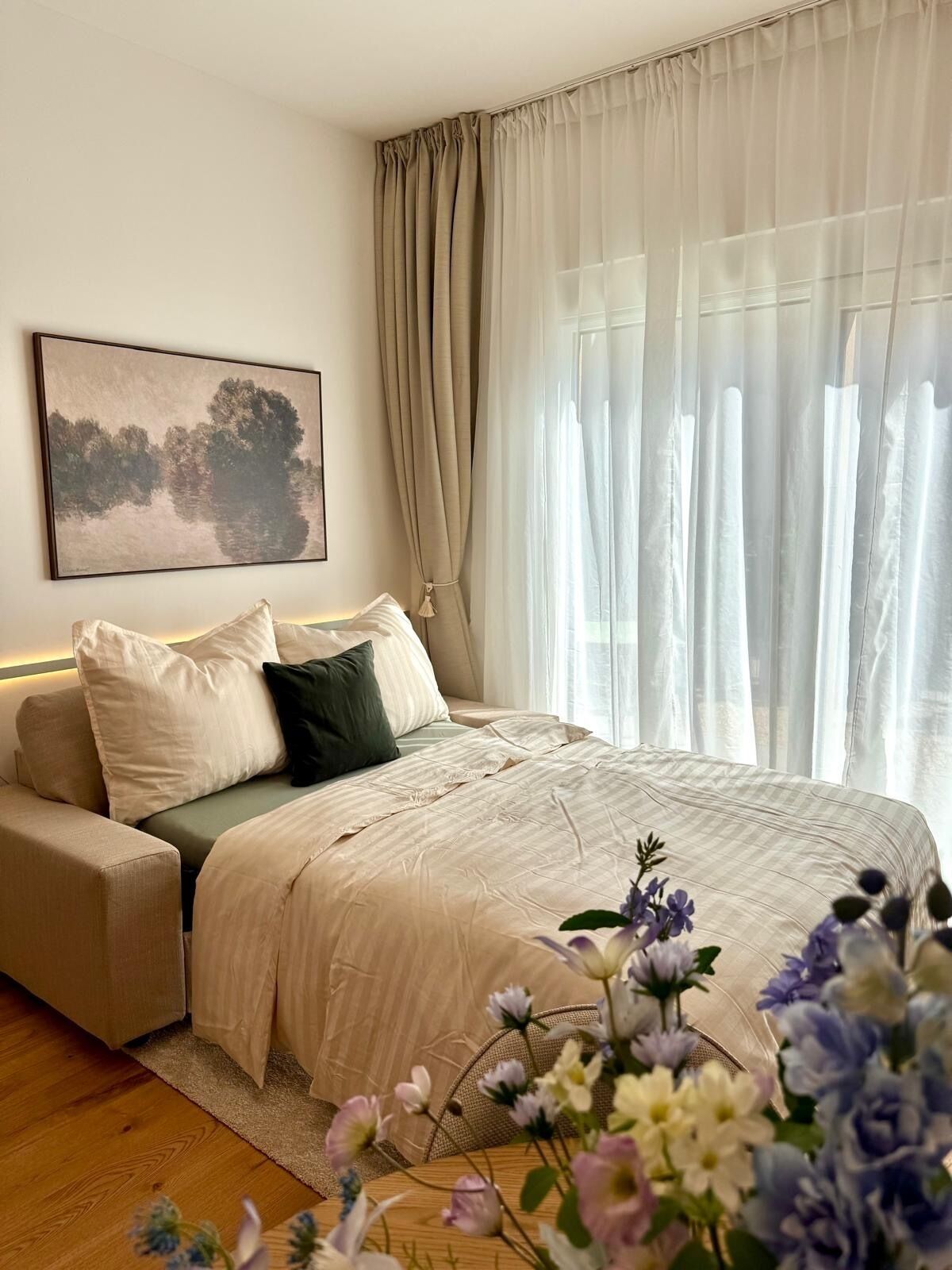 A bedroom with a bed, a sofa, a painting, and a window with curtains.