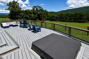 Eine Terrasse mit Sitzgelegenheiten im Freien, einem überdachten Bereich und Blick auf eine grüne Landschaft mit Bäumen und Hügeln.