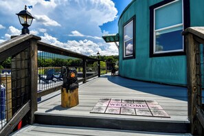 Una terrassa de fusta amb un rètol que diu 'WELCOME', una escultura d'ós negre i un edifici turquesa amb una finestra.