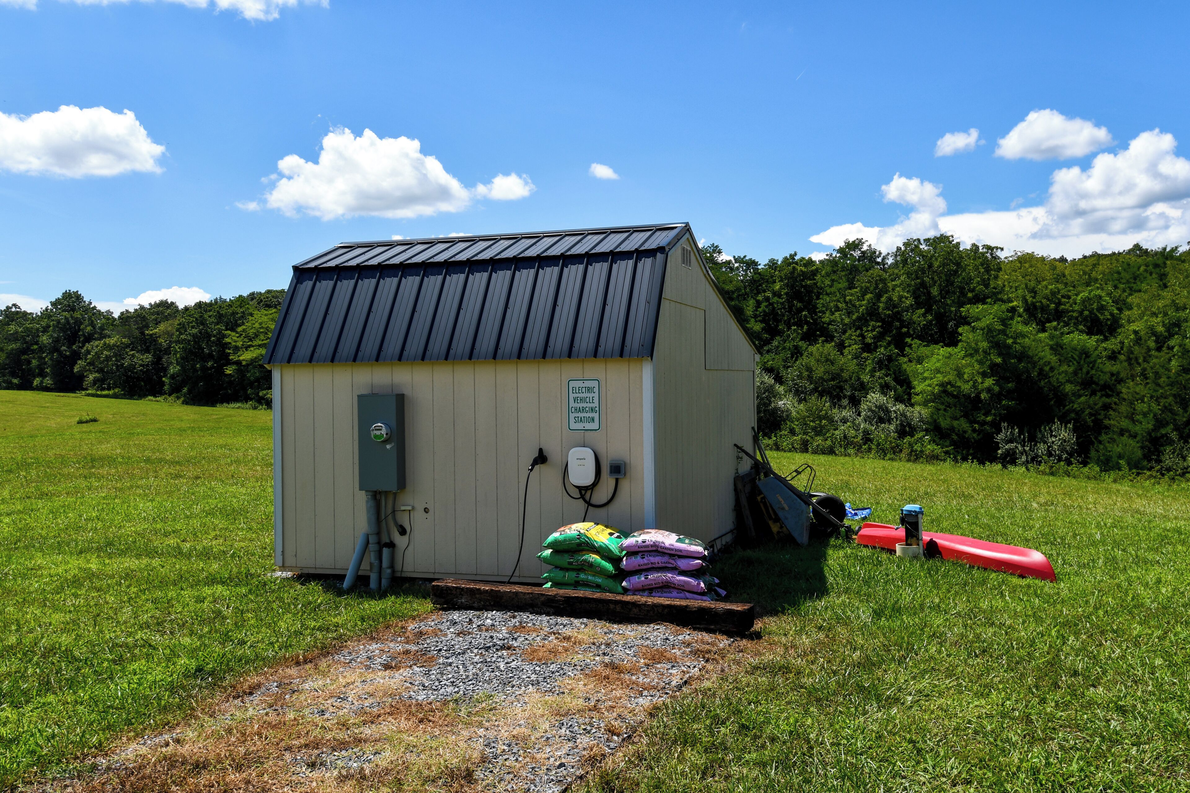 A small utility shed with a metal roof, a charging station, and bags of garden soil.