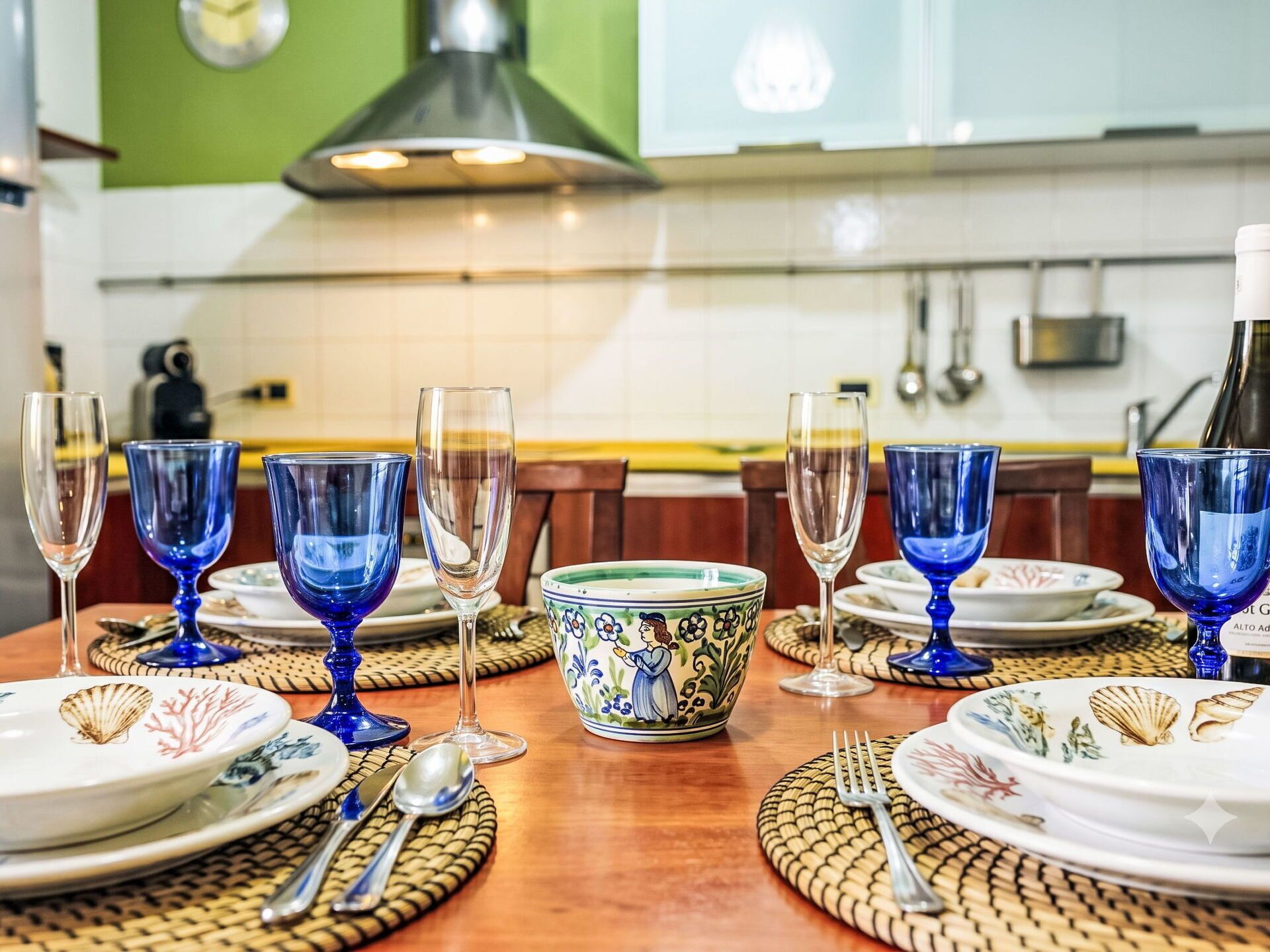A dining table set with blue glassware and white plates, with a decorative bowl in the center.