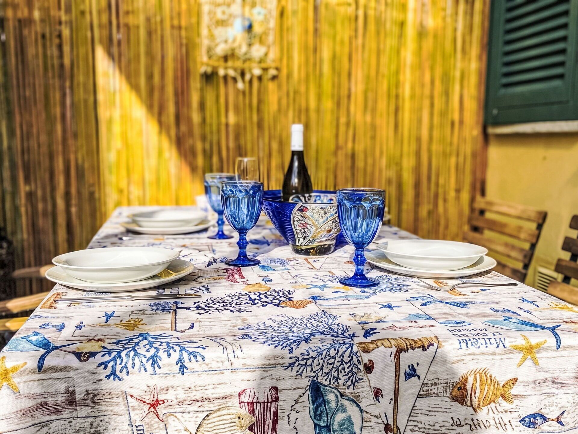 Una mesa de comedor con cristalería azul y platos, con un fondo de bambú.