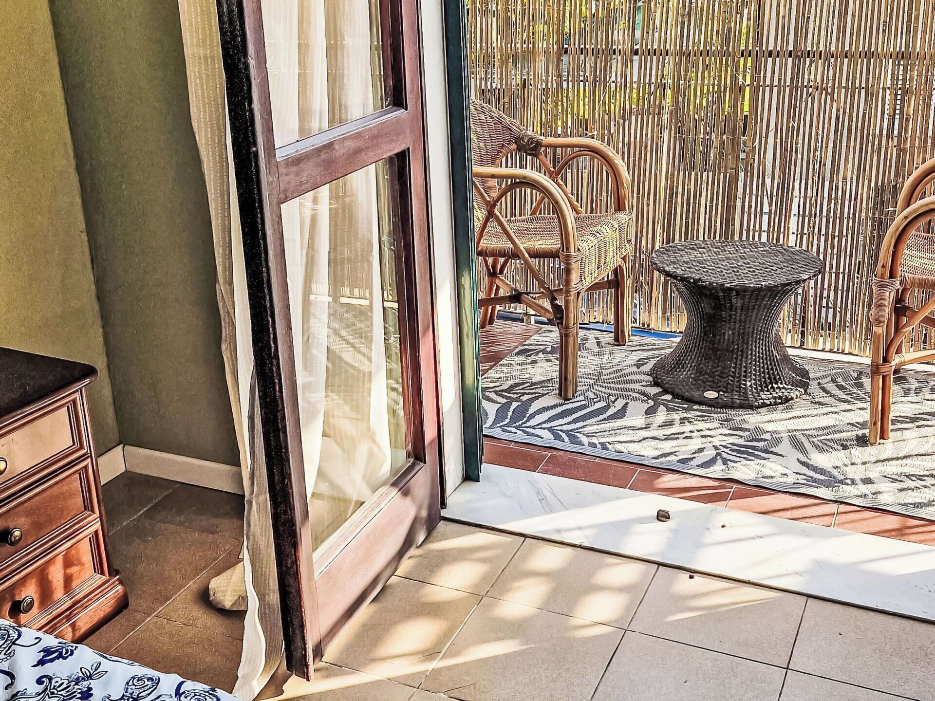 An open sliding glass door leading to an outdoor patio area with wicker furniture and a patterned rug.