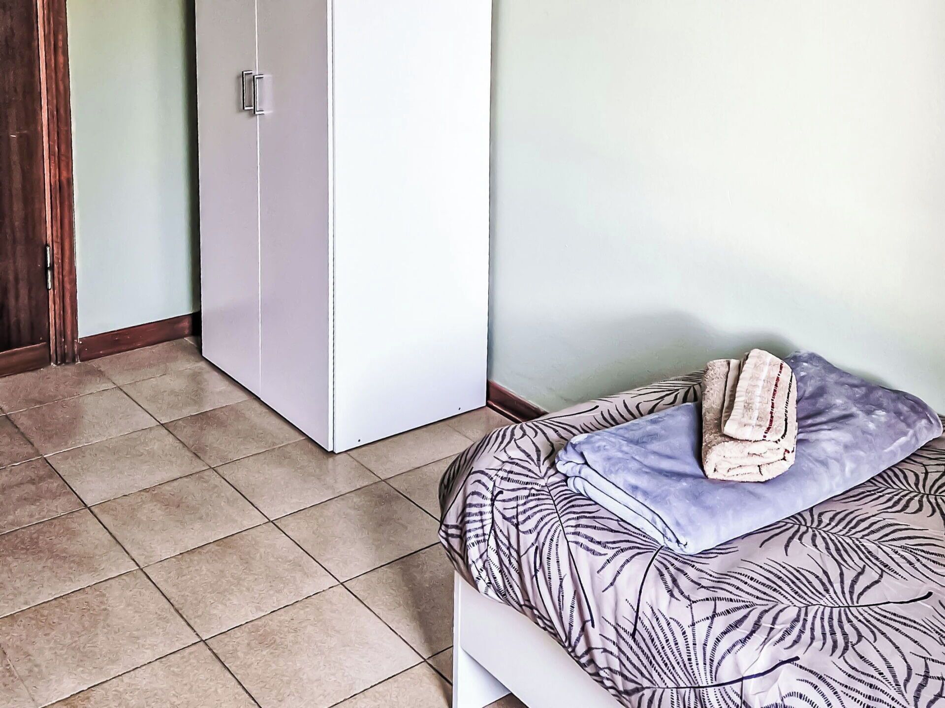 Ein Schlafzimmer mit einem Bett, einem Kopfkissen, einem gefalteten Handtuch und einem Kleiderschrank.