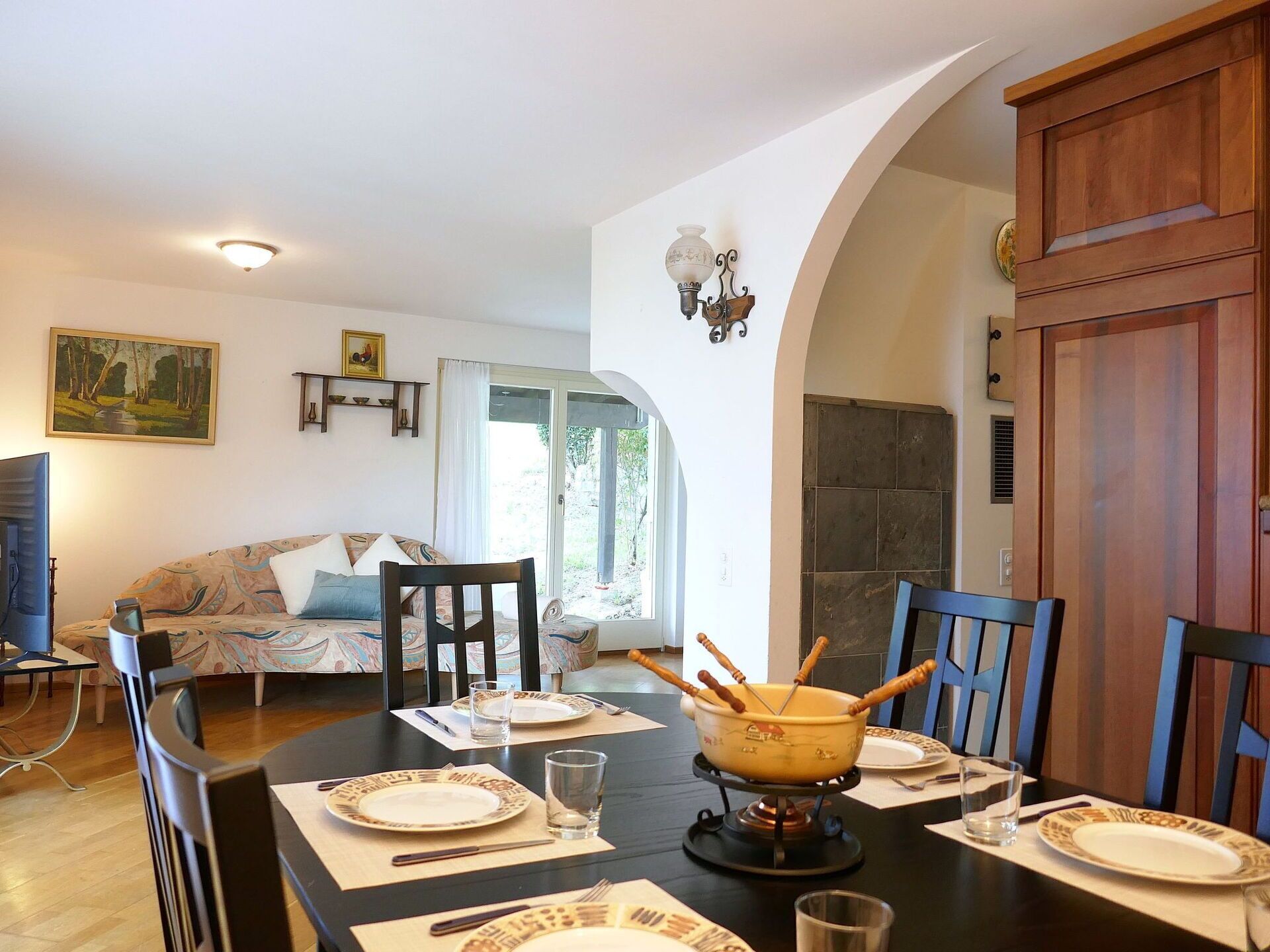 Un coin repas avec une table dressée pour quatre personnes, des chaises, un saladier contenant des couverts et un tableau accroché au mur.