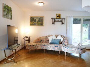 Ein Wohnzimmer mit einer Couch, einem Fernseher, einer Lampe und einem Bild an der Wand.