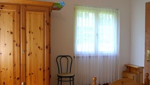 Una camera da letto con un'armadiatura in legno, un letto, una sedia e una finestra con tende leggere.