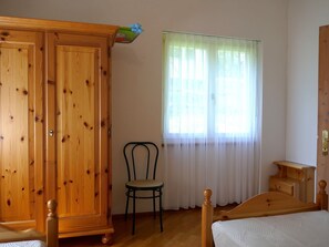 Ein Schlafzimmer mit einem Holzschrank, einem Bett, einem Sessel und einem Fenster mit transparenten Vorhängen.