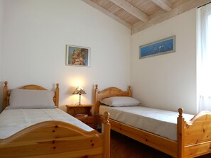 Una habitación con dos camas de madera, una mesita de noche con lámpara y un cuadro en la pared.