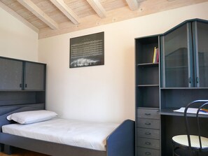 Ein Schlafzimmer mit einem Bett, einem Schreibtisch mit Schubladen, einem Sessel und einem an der Wand befestigten Schrank.