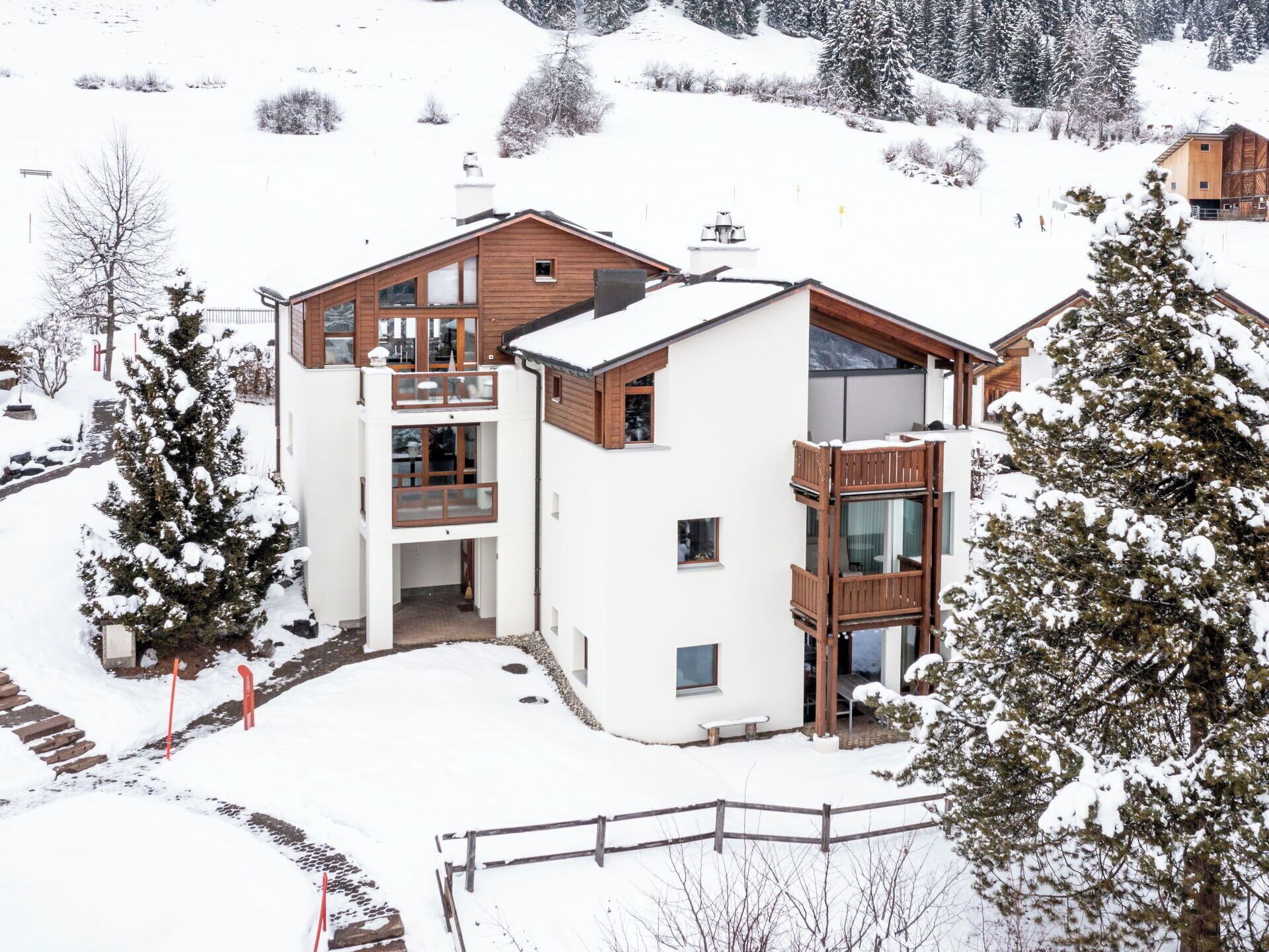 A modern two-story building with a wooden facade and large windows, surrounded by snow-covered trees and a clear sky.