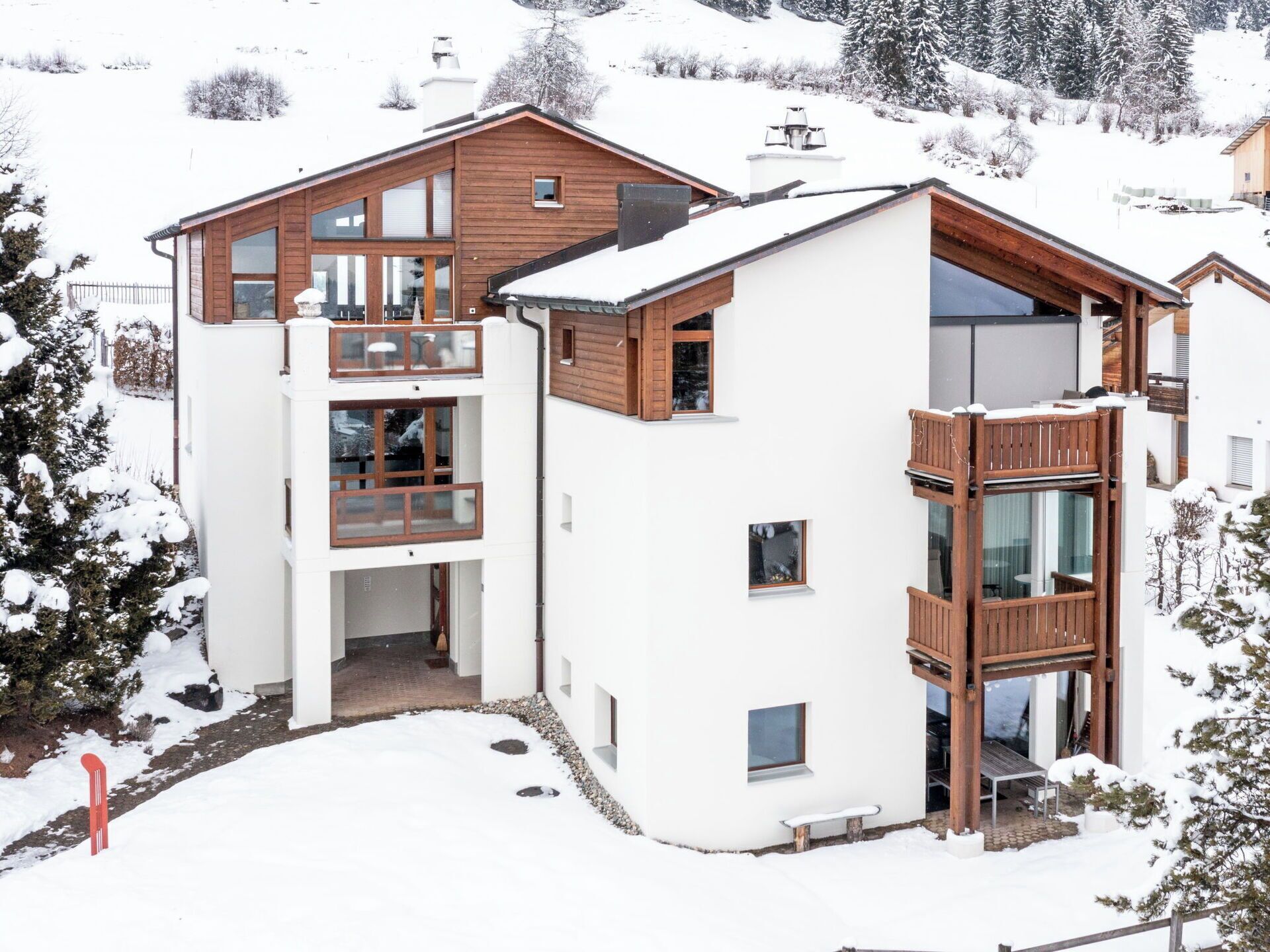 Un bâtiment moderne à plusieurs étages, doté de balcons en bois et de grandes fenêtres, et entouré d’un paysage enneigé.