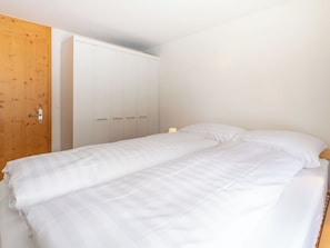 A single-bed room with a wooden door, white wardrobe, and a bedside table with a lamp.