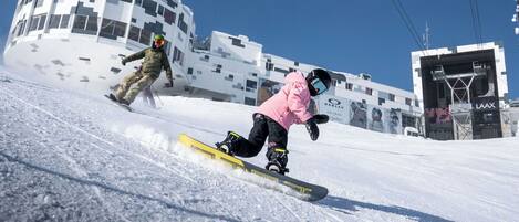 En snowboardåkare på en snötäckt sluttning med en byggnad i bakgrunden.