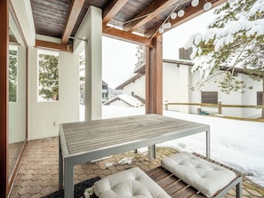 An outdoor seating area with a table and benches, surrounded by snow-covered ground and trees.