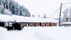 A wooden cabin with a snow-covered roof, surrounded by snow-covered ground and trees.