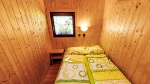 A small wooden room with a single bed, a window, and a nightstand.