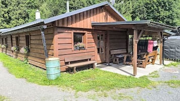 A wooden cabin with a porch, a window with flowers, and a bench.