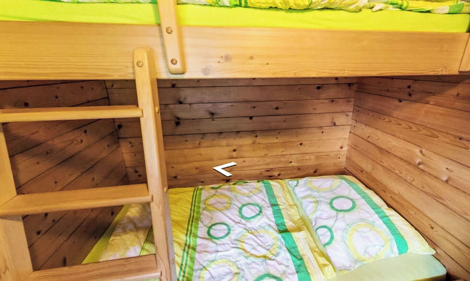 Una cama litera con escalera, paredes de madera y ropa de cama estampada.