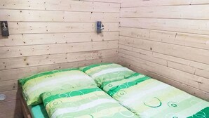 A small, single-bed room with wooden walls and a simple bed with green and white bedding.