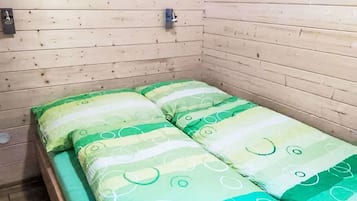A small, single-bed room with wooden walls and a simple bed with green and white bedding.
