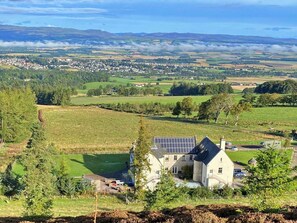 Ein Landhaus mit Solaranlage, umgeben von grünen Feldern und einem entfernten Dorf.