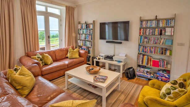 Ein Wohnzimmer mit braunem Ledersofa, einem Couchtisch, einem Bücherregal und einem Fernseher.