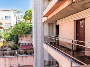 Ein modernes Gebäude mit Balkon, Tür und Blick auf die umliegende Landschaft mit Bäumen und weiteren Gebäuden.