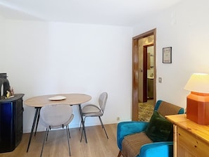 Une petite pièce meublée, avec une table ronde, deux chaises, un canapé, une lampe et une porte donnant sur une autre pièce.