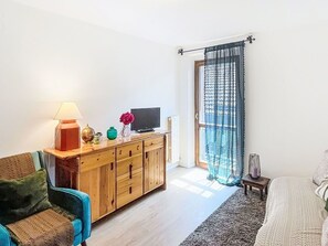 Ein Zimmer mit einem Holzschrank, einem Fernseher, einem Sessel und einem Bett.