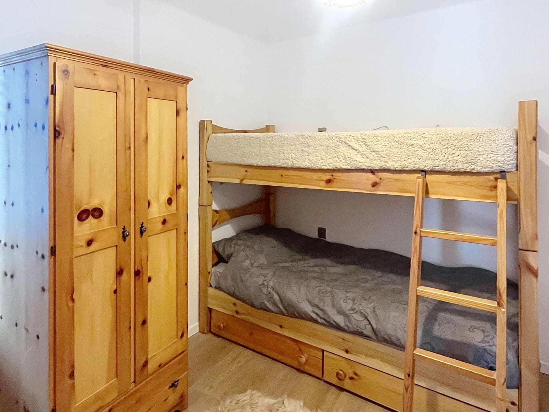 A bunk bed with a wooden frame and a storage cabinet with two doors.