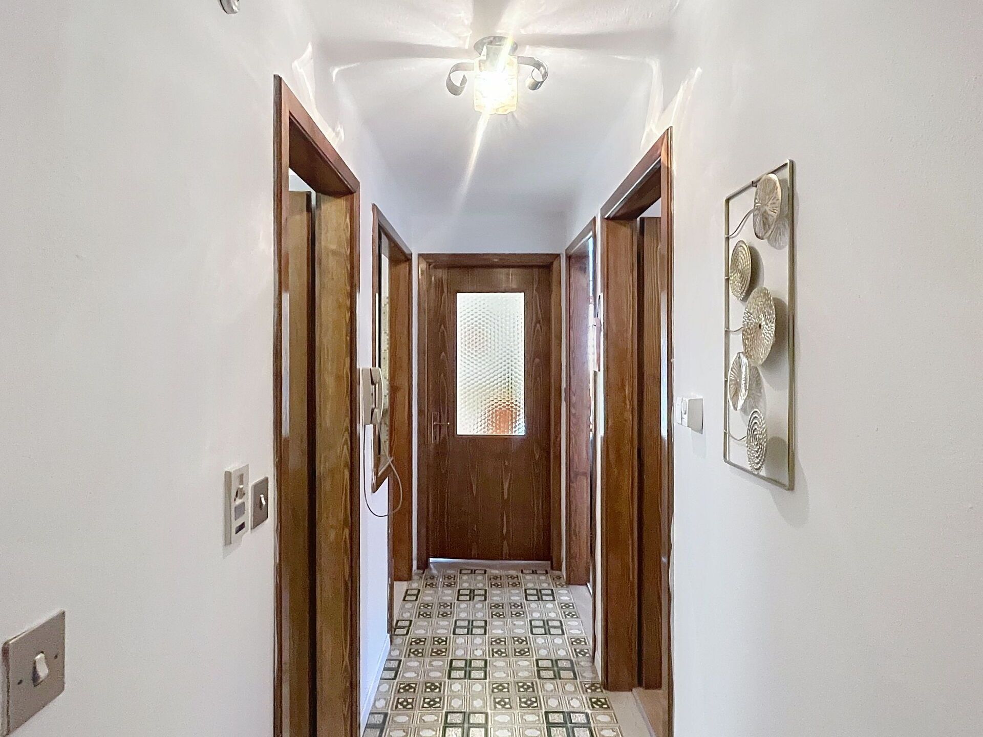 A hallway with a patterned floor, wooden doors, and a ceiling light fixture.