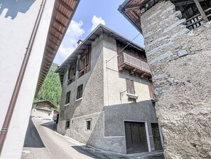 Eine enge Gasse mit Steinbauten, eines davon mit Balkon und Fensterläden, das andere mit einer Holztür.