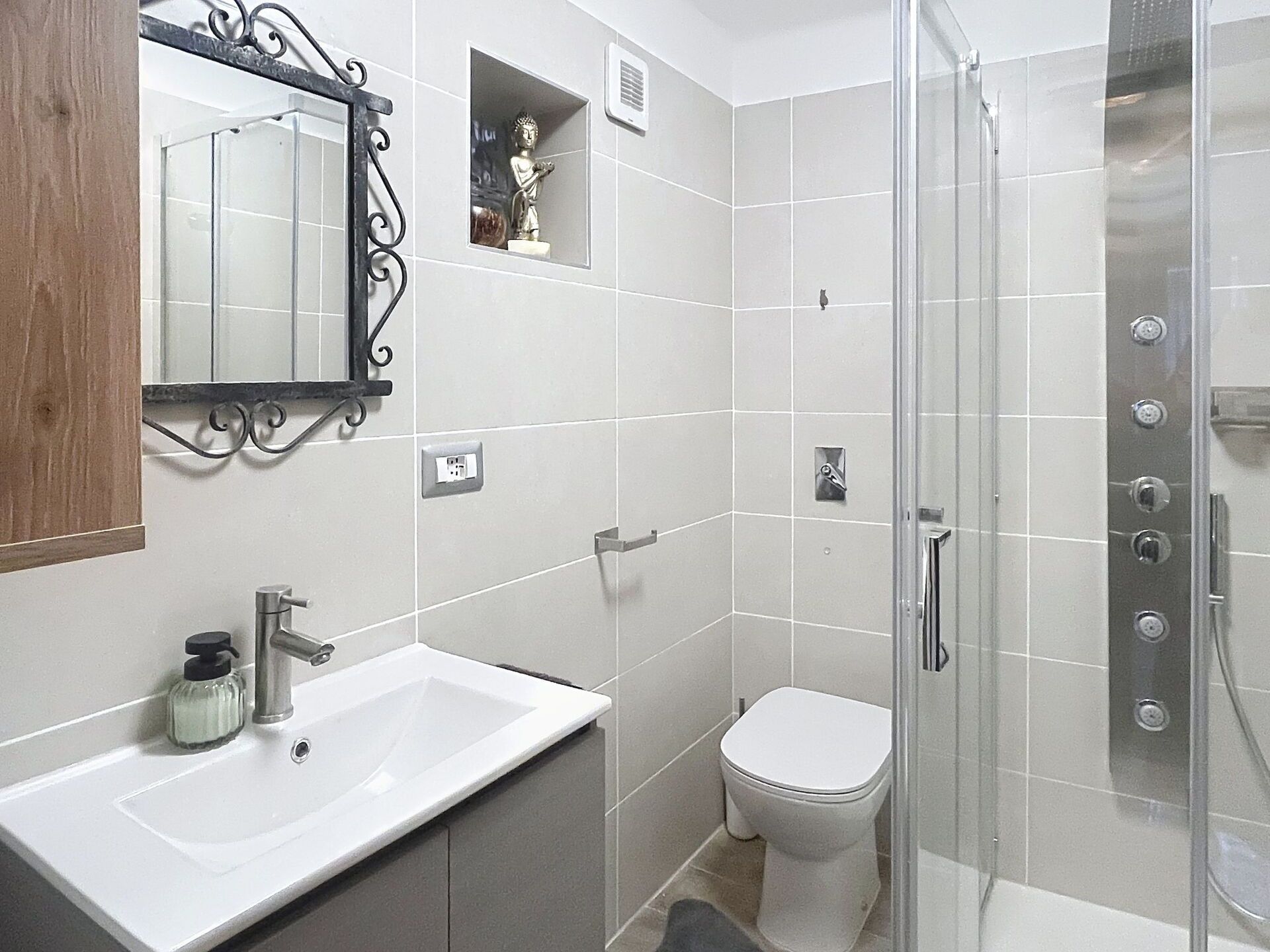 Een badkamer met een wit wastafelmeubel, een toilet en een douche met glazen wanden.