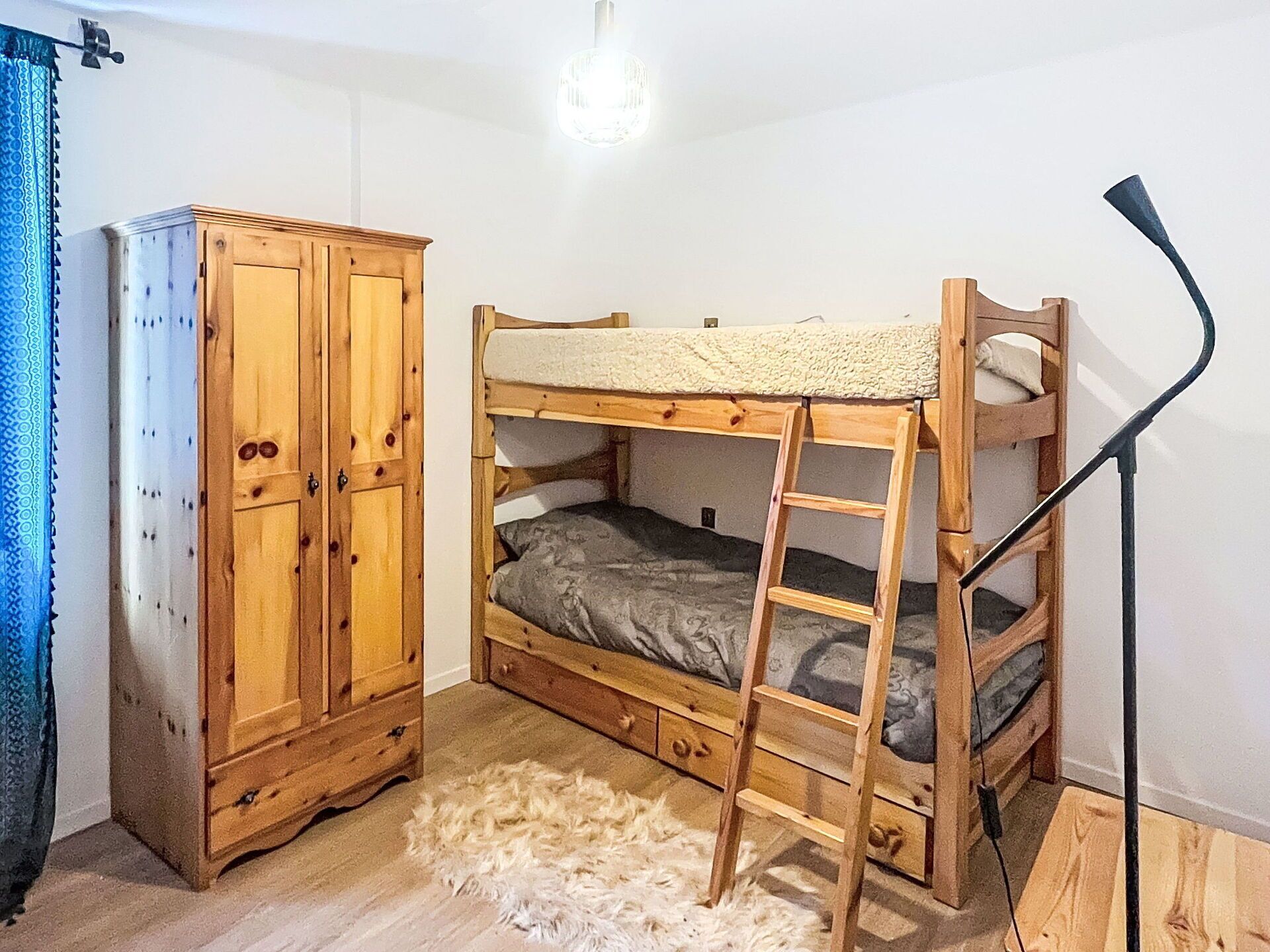 Una cama individual con escalera, un armario y una lámpara en una habitación con piso blanco y un tapete mullido.