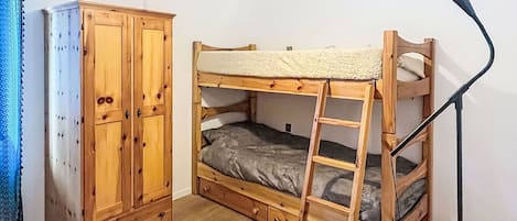 A bunk bed with a ladder, a wardrobe, and a lamp in a room with a white floor and a fluffy rug.
