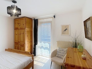 Une chambre avec une armoire en bois, un lit, une table avec un vase et un tableau encadré au mur.
