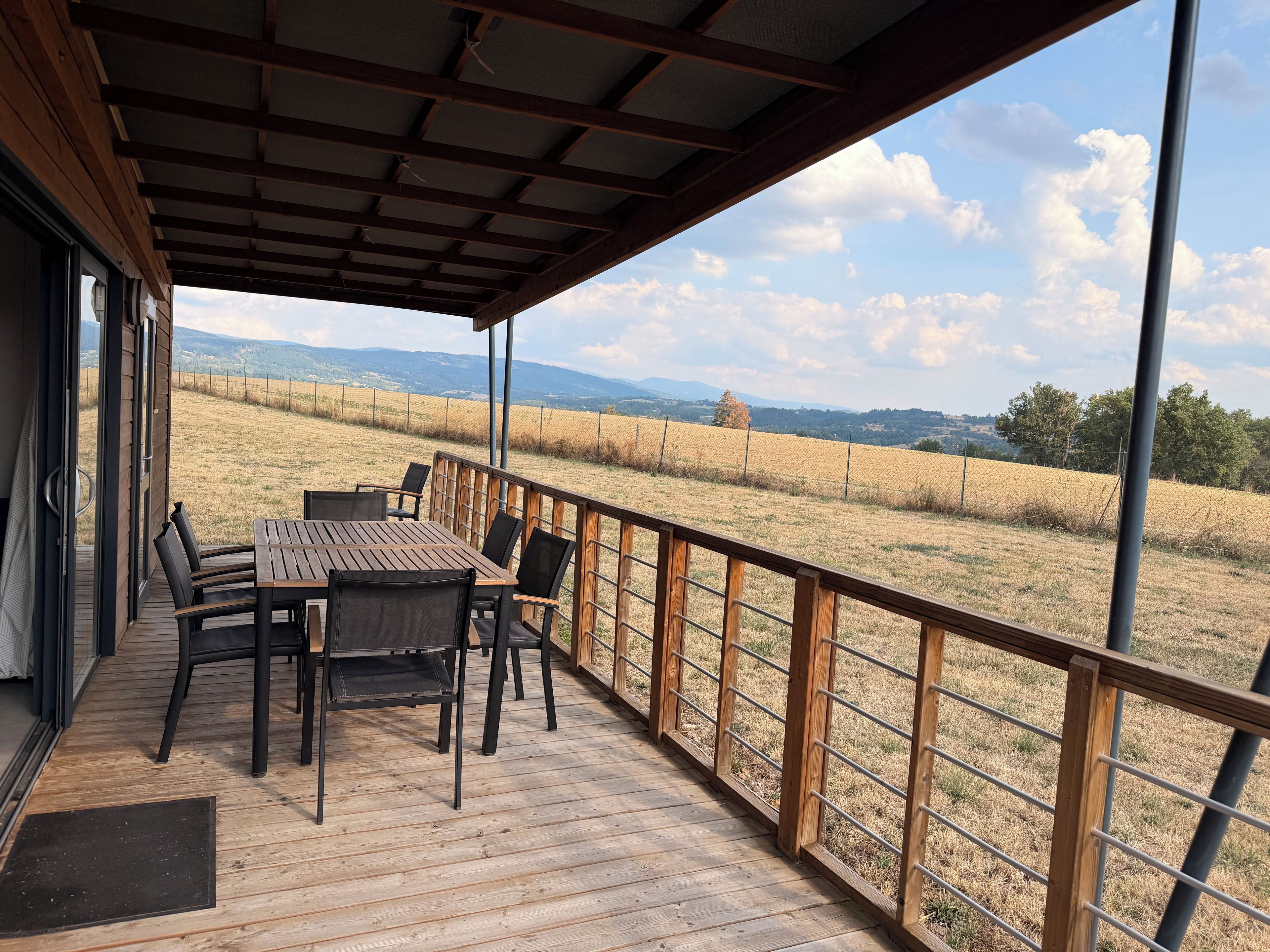 A covered outdoor seating area with a table and chairs, overlooking a field and distant hills.