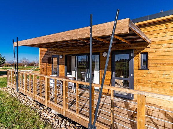 Una cabaña de madera con terraza, asientos exteriores y un patio cubierto.