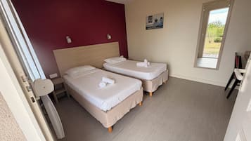 A hotel room with two beds, a red accent wall, a small window, and a door.