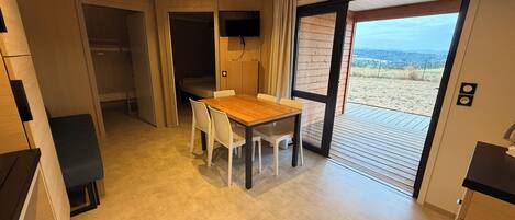 A modern kitchen with a dining area, a TV mounted on the wall, and a sliding glass door leading to an outdoor deck.