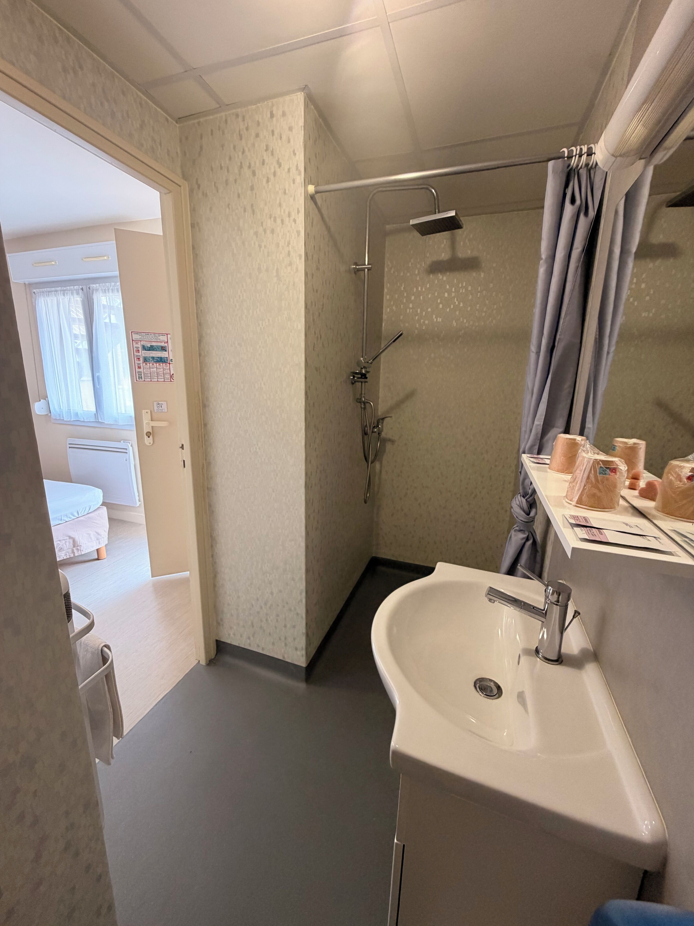 A bathroom with a shower, a sink, and a toilet. There is a towel rack and a mirror.