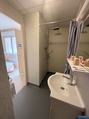 Baño con ducha, lavamanos y retrete. Hay un perchero y un espejo.