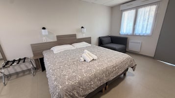 A hotel room with a bed, bedside lamps, a chair, a window with curtains, and a radiator.