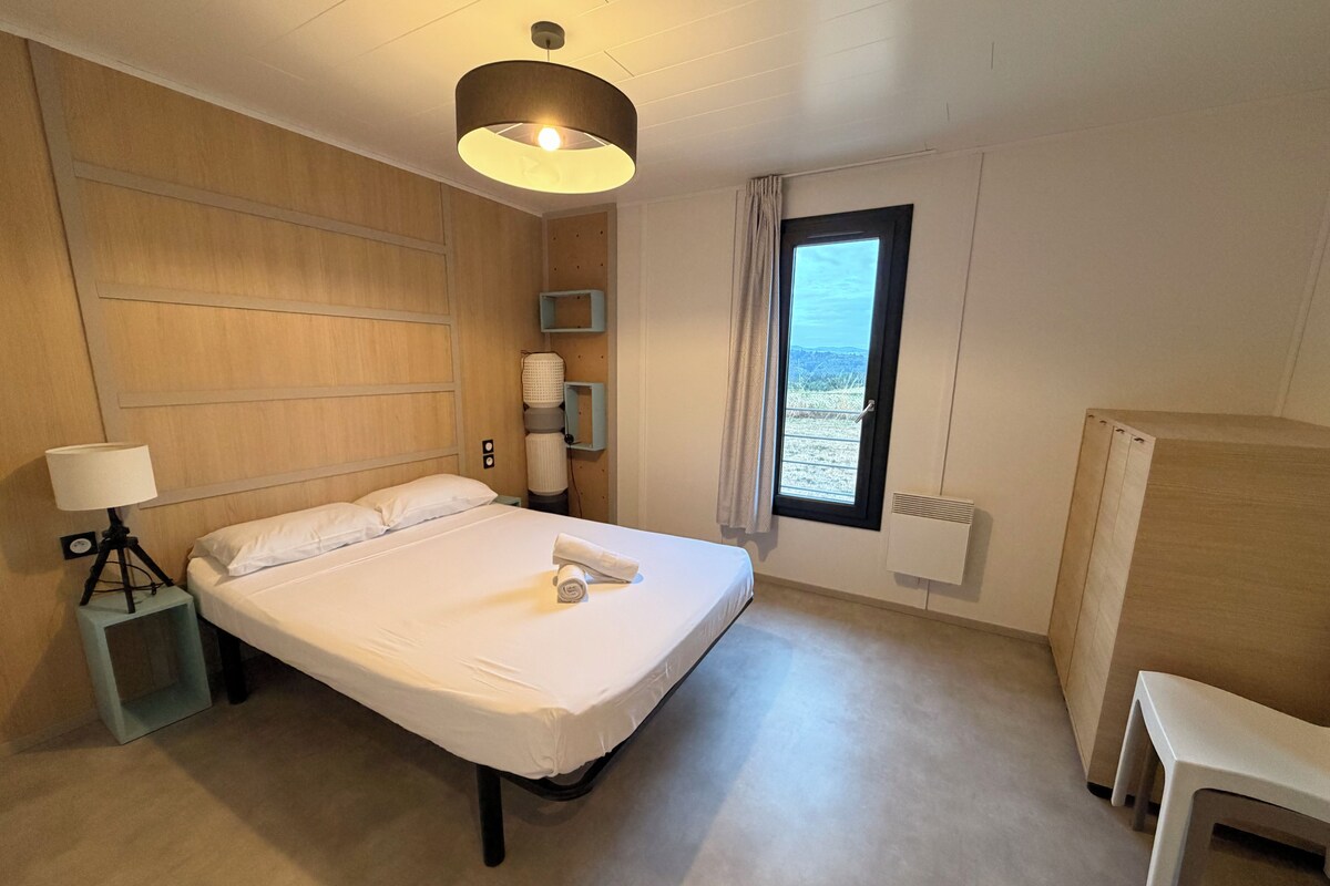 Habitación de hotel con cama, lámpara de noche, ventana y vista al exterior.