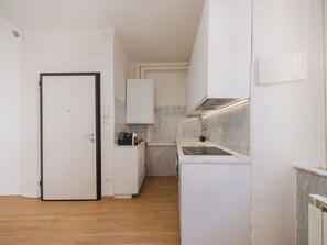 Een kleine keuken met witte kastjes, een inbouwoven en een magnetron.