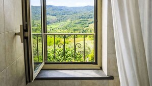 Ein Fenster mit Blick auf eine grüne Landschaft, einem Metall-Balkongeländer und einem weißen Vorhang.